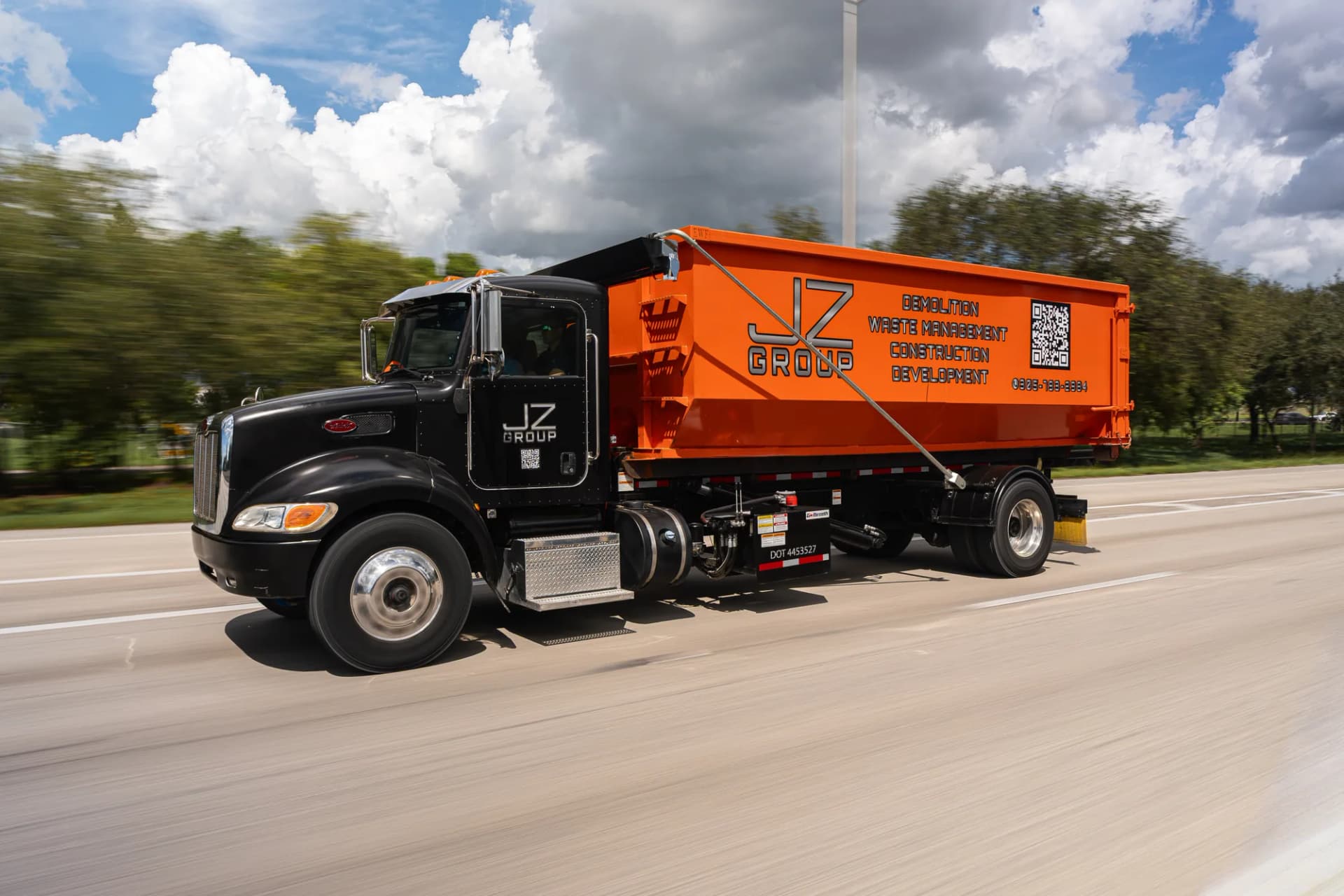 JZ branded hauling truck carrying an orange roll-off container